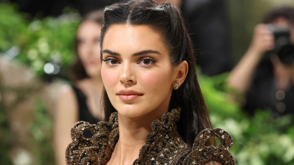 Kendall Jenner poses at the Met Gala wearing a brown gown. Her hair is styled half up.